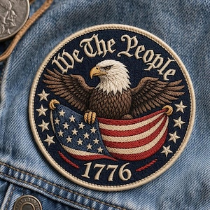 May include: Circular embroidered patch with a bald eagle and American flag design. The text "We The People" and the year "1776" are displayed on a navy blue background. The eagle has a white head and brown body, with the flag in red, white, and blue.