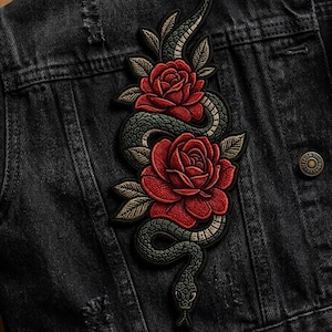 May include: Embroidered patch featuring a green snake entwined with two red roses and green leaves. The patch is sewn onto a black denim jacket. The snake has a detailed scale pattern, and the roses are in full bloom.