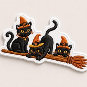 May include: An embroidered patch featuring three black cats with yellow eyes, each wearing an orange witch hat with a brown star. The cats are positioned on a brown broomstick, with one cat sitting, one crouching, and one peeking over the handle.