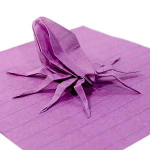 May include: A purple origami spider with eight legs, sitting on a purple lined paper.