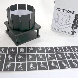 May include: A black and white zoetrope with a skeleton animation. The zoetrope is made of cardboard and has a black base. The animation is of a skeleton sitting down and getting up. The zoetrope is labelled "ZOETROPE 1929".