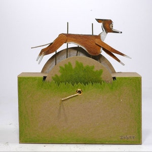 May include: A brown and white paper mache dog sculpture running on a wheel with green grass at the bottom. The sculpture is made by Zuber.
