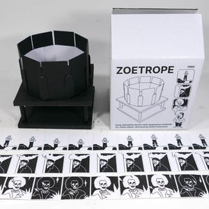 Könnte beinhalten: Ein Schwarz-Weiß-Zoetrop-Set mit einem Karton, auf dem "ZOETROPE 1990" steht. Das Set enthält ein schwarzes Papp-Zoetrop, eine Basis und einen Streifen mit 12 Schwarz-Weiß-Bildern eines Skeletts.