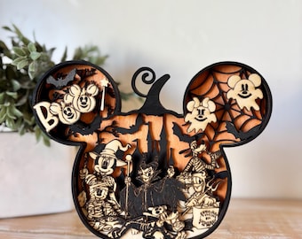 May include: Wooden Halloween decoration in the shape of Mickey Mouse's head. The layered design features spooky characters, bats, and the word "Boo". The decoration is made of natural wood with black accents.