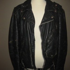 May include: Black leather jacket with a classic biker style. Features include a notched collar, asymmetrical zipper closure, multiple pockets, and silver-tone hardware. The jacket is displayed on a mannequin.