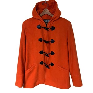May include: Orange hooded toggle coat with black toggles and a zipper closure. The coat has two pockets and the label "PAUL LE"