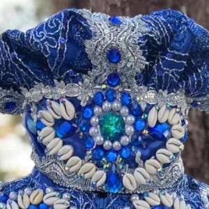 May include: A blue and silver crown with white seashells and blue jewels. The crown is made of fabric and has a ruffled edge.