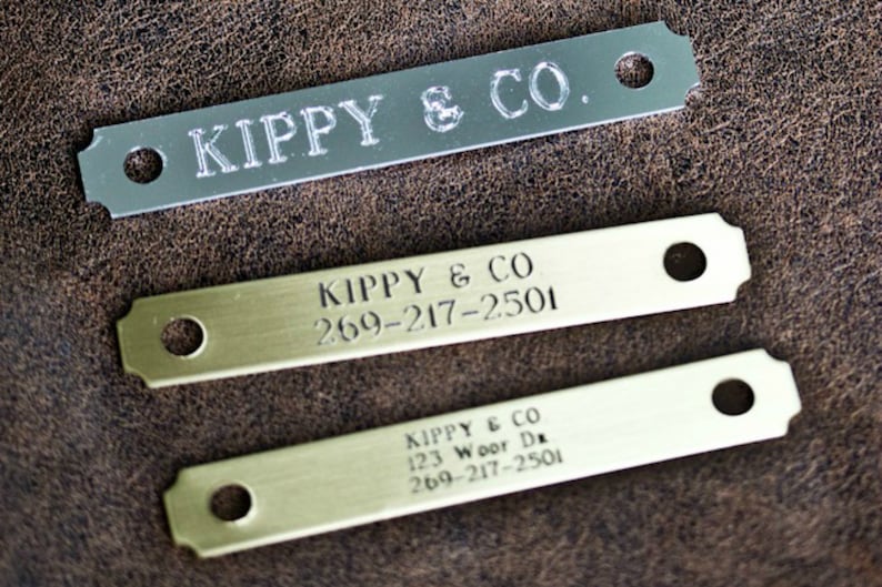 May include: Three metal dog tags with rounded edges. The top tag is silver and says "KIPPY & CO.". The middle tag is gold and says "KIPPY & CO 269-217-2501". The bottom tag is gold and says "KIPPY & CO 123 Woor Da 269-217-2501".