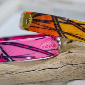 K&ouml;nnte beinhalten: Zwei Hundehalsb&auml;nder mit einem Tarnmuster. Das obere Halsband ist orange und schwarz, das untere Halsband ist pink und schwarz. Beide Halsb&auml;nder haben den Schriftzug "Biothane" aufgedruckt.