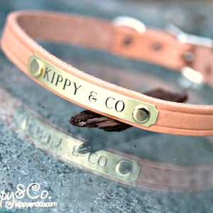 May include: A light pink leather dog collar with a gold metal plate engraved with the text "KIPPY & CO."