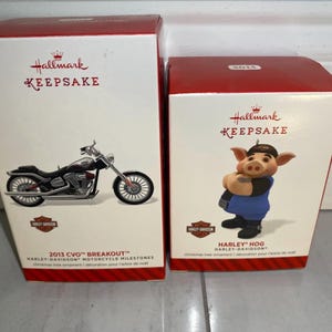 May include: Two Hallmark Keepsake Christmas ornaments. The first ornament is a red, white, and black Harley-Davidson motorcycle. The second ornament is a red, white, and blue pig wearing a Harley-Davidson shirt. Both ornaments have the Hallmark Keepsake logo.