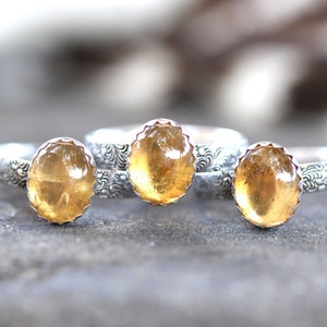 May include: Three silver rings with yellow gemstone settings. The rings have a decorative floral pattern.