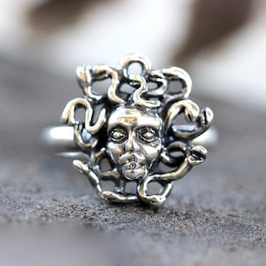 Puede incluir: Un anillo de plata con un dise&ntilde;o detallado de la cara de Medusa rodeada de serpientes.