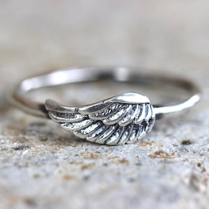 May include: A silver ring with a wing design. The wing is detailed with lines and has a textured finish.
