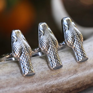 May include: Three silver snake head rings. The rings are stacked on top of each other and are made of a detailed snake head design.