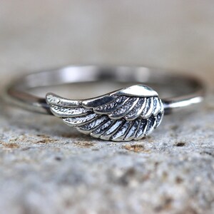 May include: A silver ring with a wing design. The wing is detailed with lines and is slightly curved.