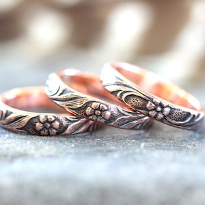 May include: Three copper rings with a floral design. The rings are stacked on top of each other.