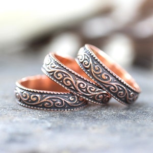 May include: Three copper rings with a decorative, swirling pattern. The rings are stacked on top of each other.