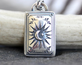 May include: Silver pendant charm featuring a tarot card design with the number XIX and a crescent moon inside a sunburst.