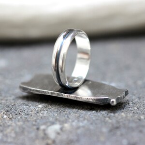 May include: A silver ring with a black band around the center. The ring is sitting on a gray surface.