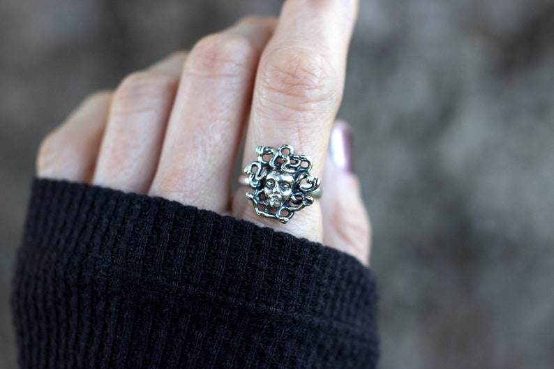 Puede incluir: Un anillo de plata con un dise&ntilde;o detallado de la cabeza de Medusa con serpientes como cabello.