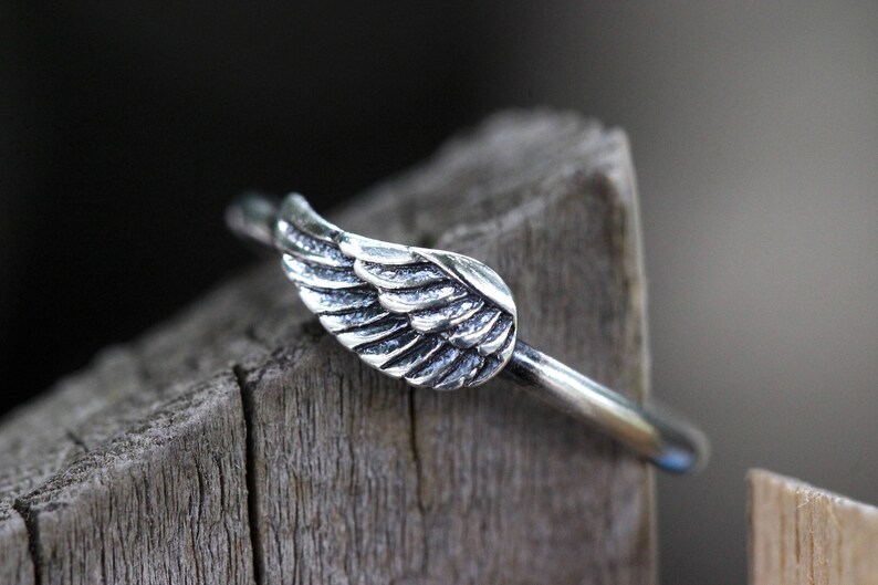 May include: A silver ring with a wing design. The ring is on a wooden surface.