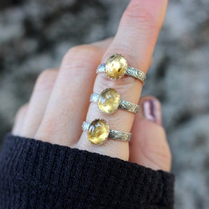 May include: Three silver rings with yellow gemstones. Each ring has a detailed floral design on the band.