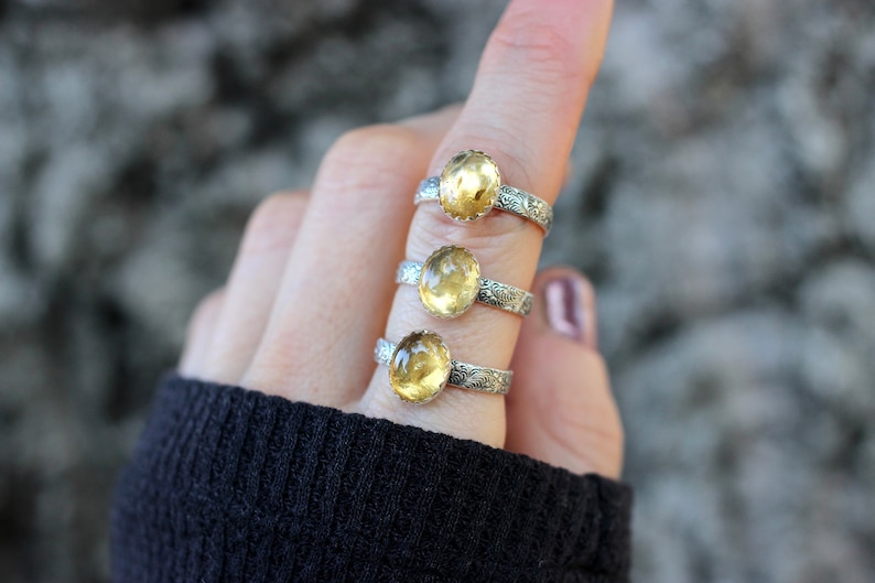 May include: Three silver rings with yellow gemstones. Each ring has a detailed floral design on the band.