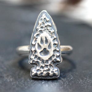 Op de afbeelding: Een zilveren ring met een getextureerd pijlpuntontwerp met een beerpootafdruk.