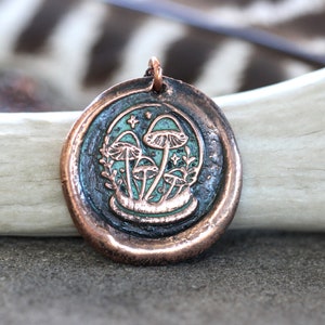 May include: A copper pendant with a green and white enamel design of mushrooms in a forest setting.