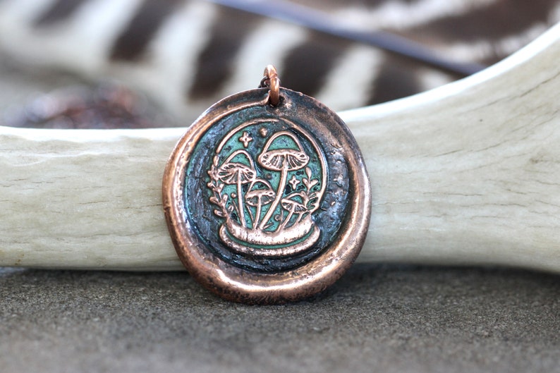 May include: A copper pendant with a green and white enamel design of mushrooms in a forest setting.
