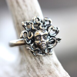 Puede incluir: Un anillo de plata con una escultura detallada de la cabeza de Medusa con serpientes como cabello.