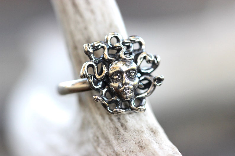 Puede incluir: Un anillo de plata con una escultura detallada de la cabeza de Medusa con serpientes como cabello.