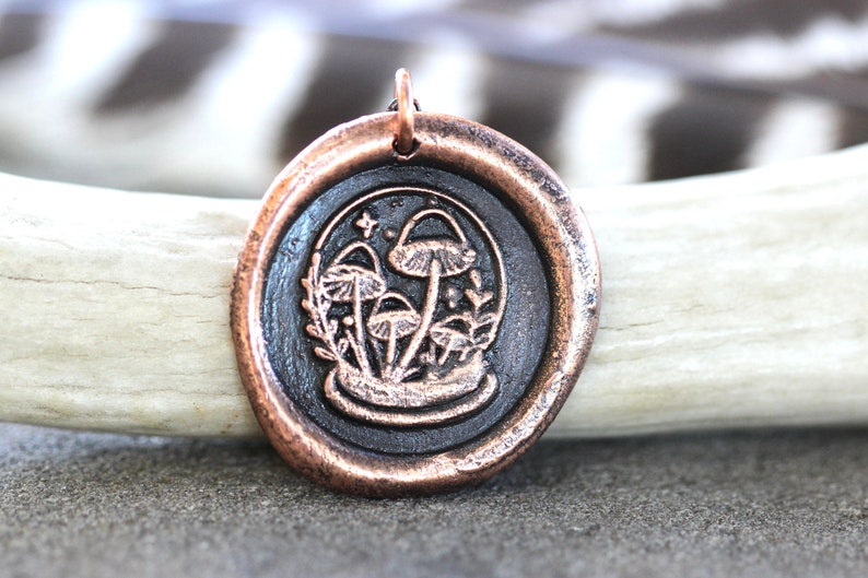 May include: A copper pendant with a black wax seal featuring a detailed illustration of mushrooms and foliage.