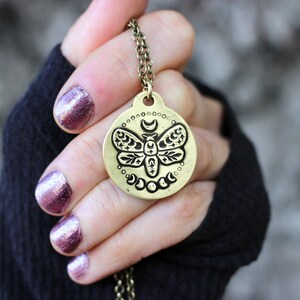 Peut inclure: Un collier en or avec un pendentif rond repr&eacute;sentant un motif de papillon de nuit d&eacute;taill&eacute; entour&eacute; d'un croissant de lune et d'&eacute;toiles.