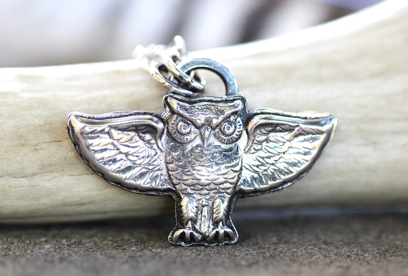 May include: Silver owl pendant with spread wings, detailed with textured feathers and large, round eyes. The pendant is attached to a silver chain.