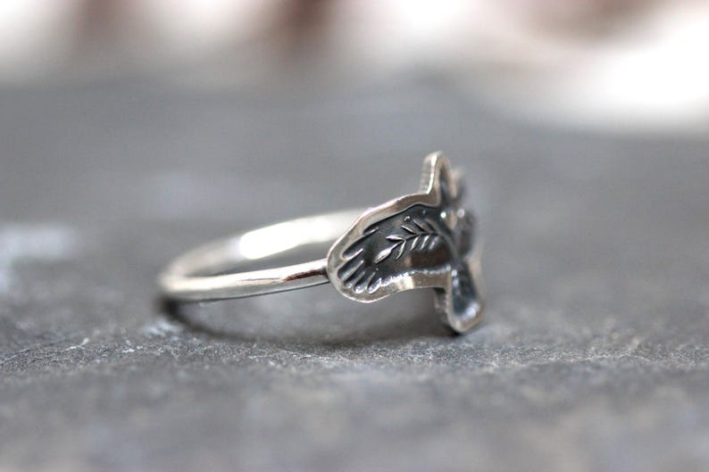 May include: A silver ring with a leaf design. The ring has a thin band and a detailed leaf motif on the face. The ring is shown on a gray surface.