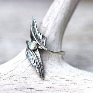 May include: A silver ring with two feather designs and a white opal gemstone in the center.