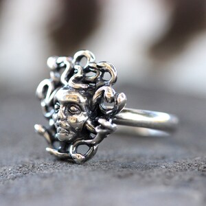 Puede incluir: Un anillo de plata con un dise&ntilde;o detallado de la cabeza de Medusa con serpientes como cabello.