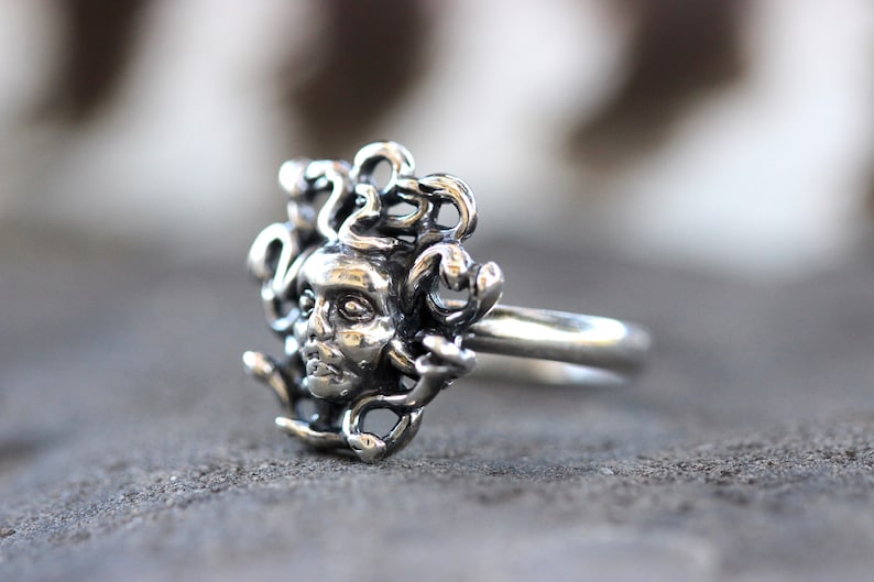 Puede incluir: Un anillo de plata con un dise&ntilde;o detallado de la cabeza de Medusa con serpientes como cabello.
