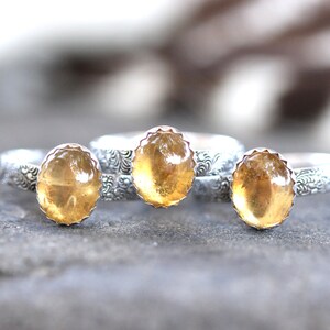 May include: Three silver rings with yellow gemstone settings. The rings have a floral design on the band.