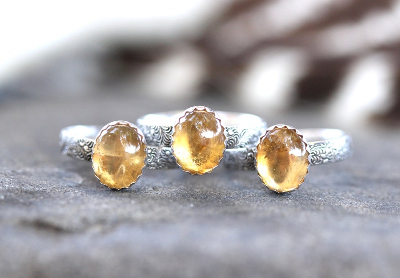 May include: Three silver rings with yellow gemstone settings. The rings have a floral design on the band.