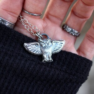 May include: A silver owl pendant necklace with a detailed design. The owl is spread-winged and has a realistic appearance.