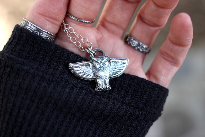 May include: A silver owl pendant necklace with a detailed design. The owl is spread-winged and has a realistic appearance.