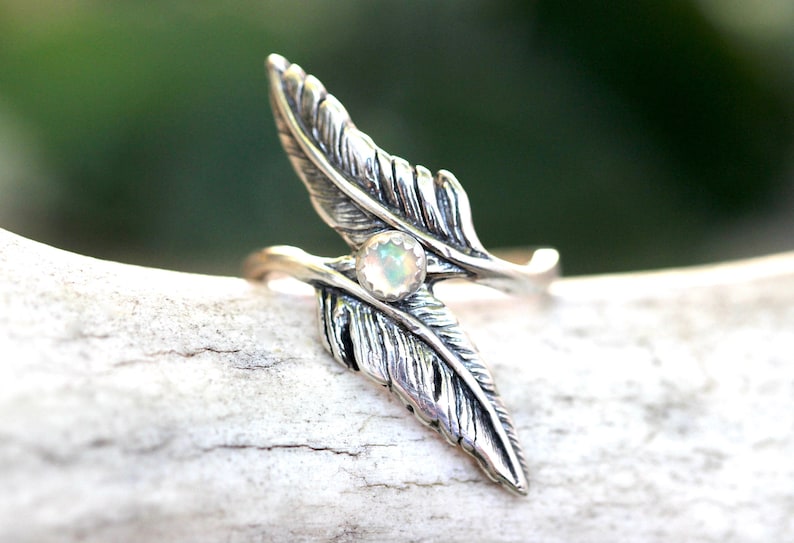 May include: A silver ring with two feather designs and a white opal gemstone in the center.