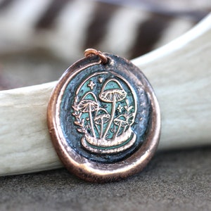 May include: A copper pendant necklace with a green enamel design of mushrooms and leaves. The pendant is round and has a textured surface.
