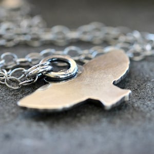 May include: A silver necklace with a bird pendant. The pendant is a simple, minimalist design with a smooth, polished finish.