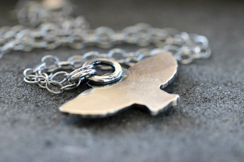 May include: A silver necklace with a bird pendant. The pendant is a simple, minimalist design with a smooth, polished finish.