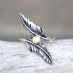 May include: A silver ring with a feather design and a small opal gemstone in the center.