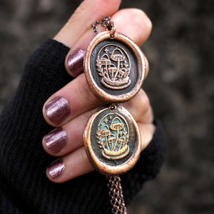 May include: A copper necklace with two round pendants featuring a design of mushrooms and stars. The pendants are connected by a copper chain.